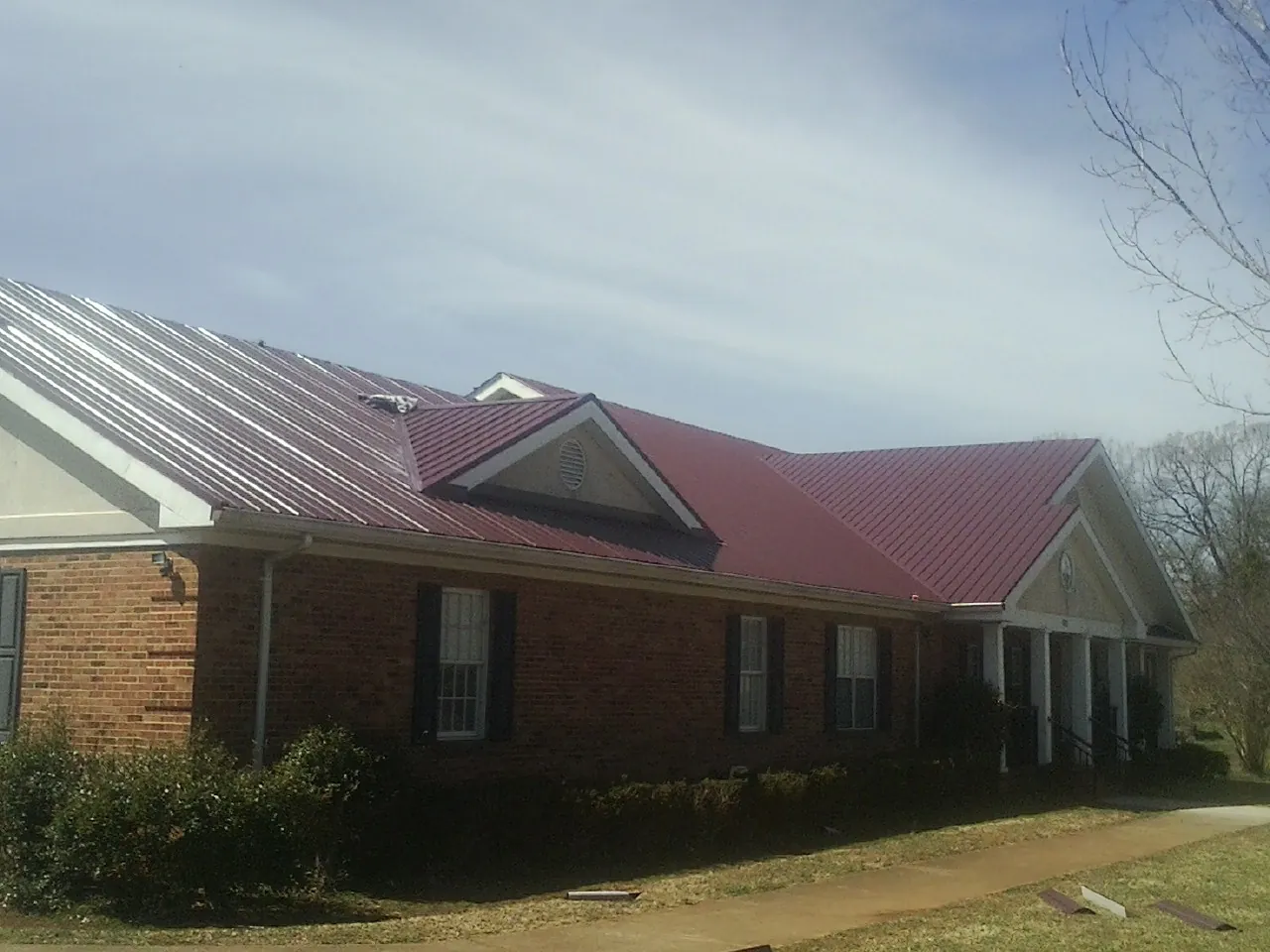 Red metal roof with gabled entries on a long brick building, from a Hail Damage Roof Repair job in Nashville