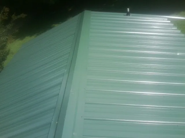 New green metal panels meeting at the ridge of a roof — Flat Roof Repair work by our crew in Nashville