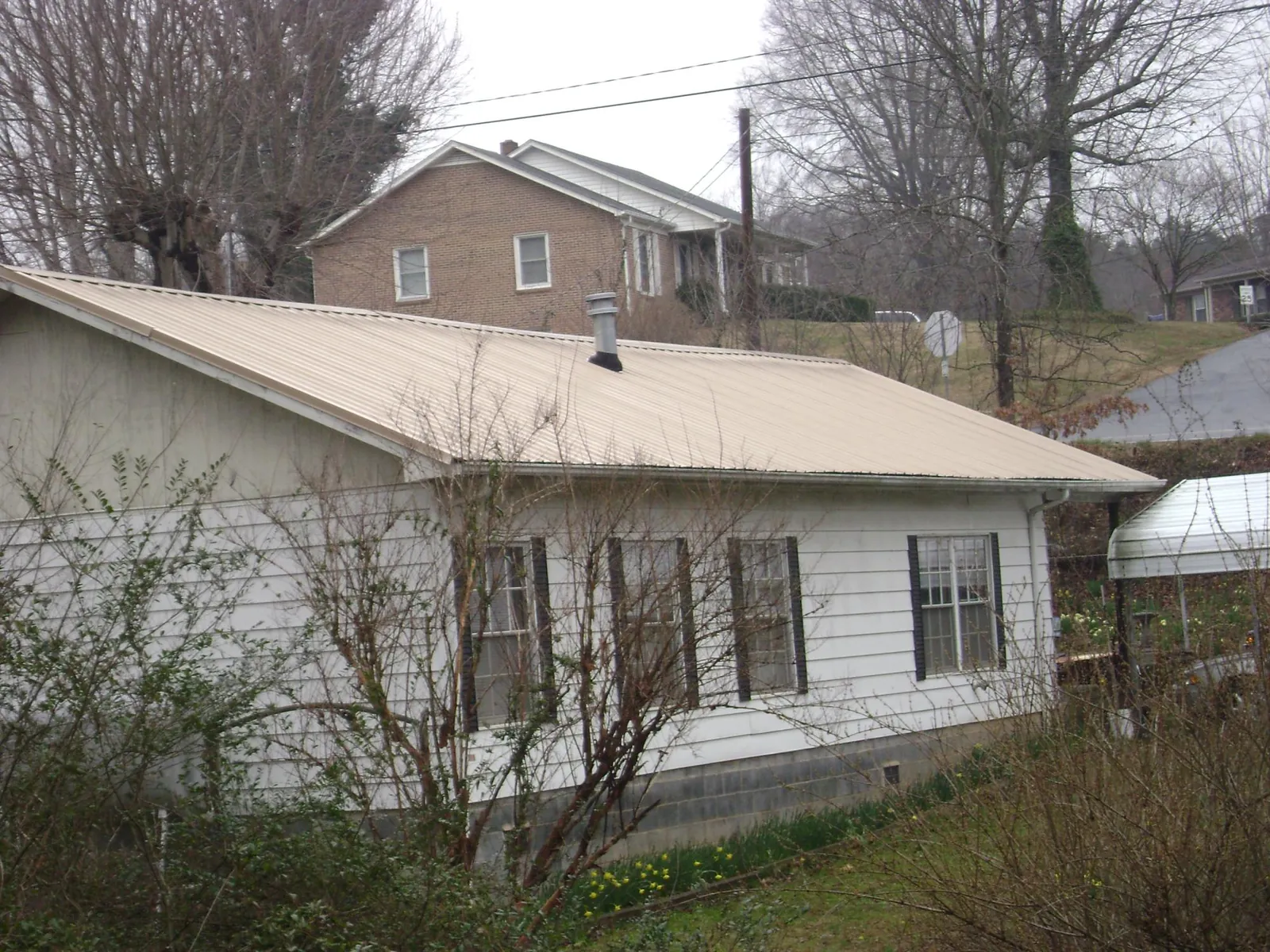 Tan metal roof on a white sided house set into a hillside — Commercial Roofing by Roofing Brothers in Nashville